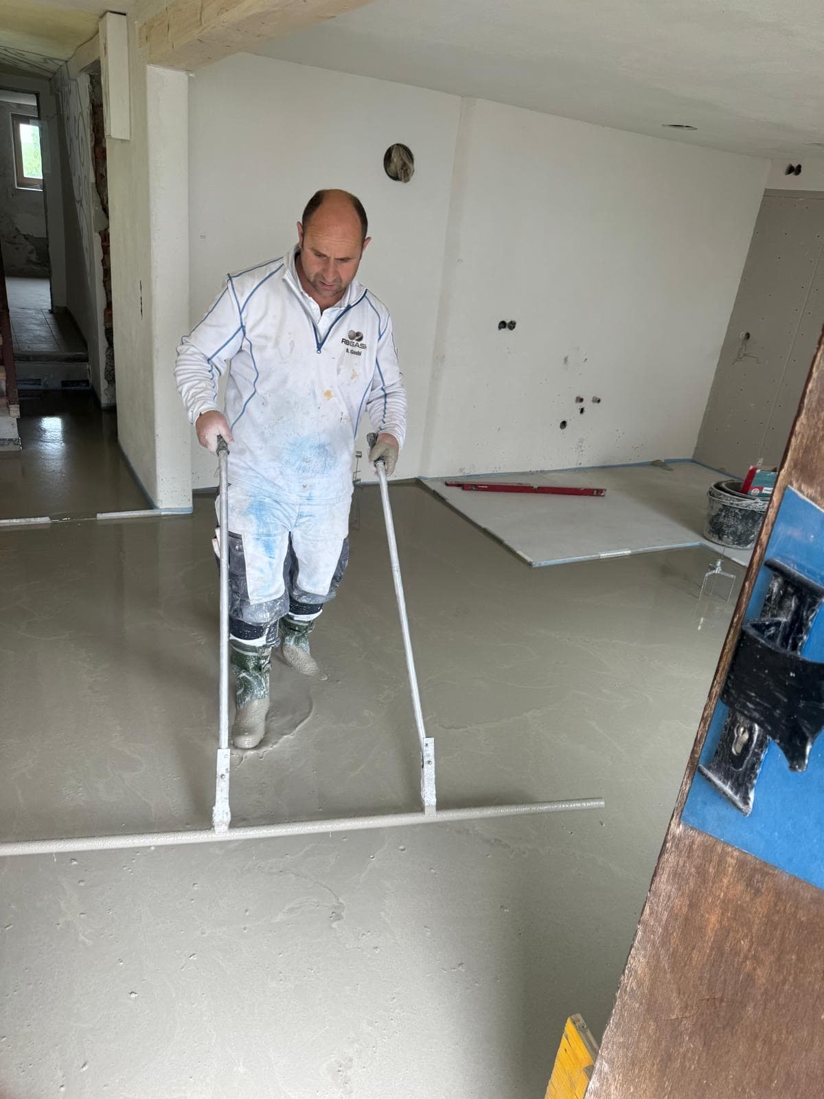 Handwerker glättet frisch verlegten Fließestrich in einem Rohbauraum